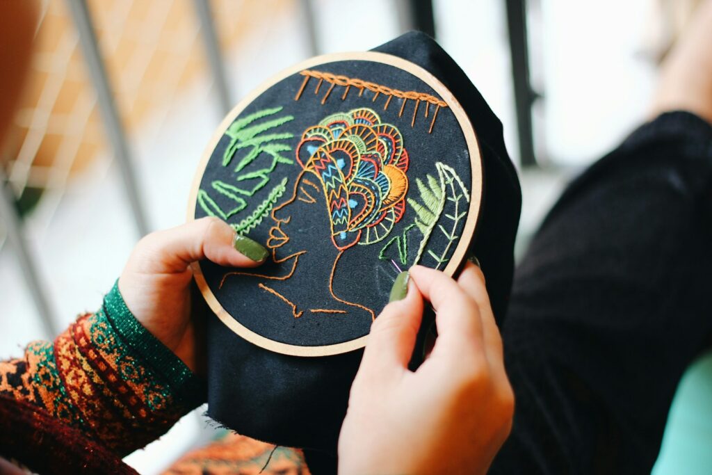 person holding embroidery hoop with colorful profile of a woman's face and headwrap with a leaf border. 